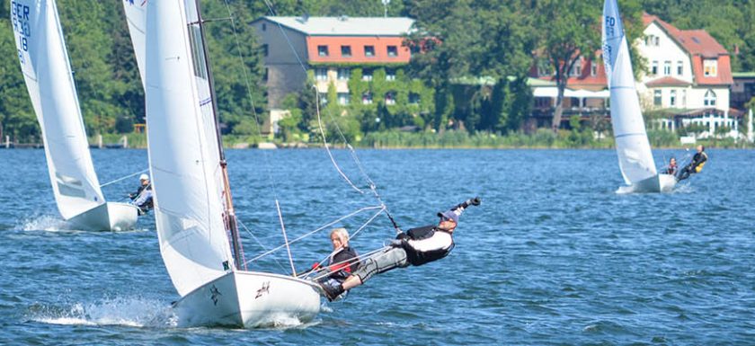 Ein Segler am Wind im Flying Dutchman (FD) beim ausreiten im Trapez, zusätzlich wird eine Hand über den Kopf gestreckt